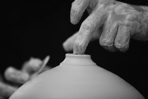 Black and white photo of a close up of hands shaping a narrow neck on a wide pot.